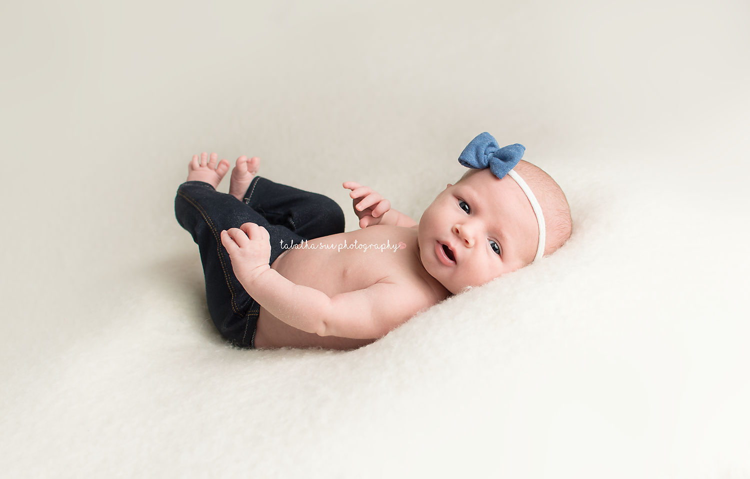 newborn-baby-girl-pictures-professional-photography-studio-in-northeast-ohio-cleveland-baby-photographer-baby-wearing-blue-bow-headband-and-tiny-jeans.png