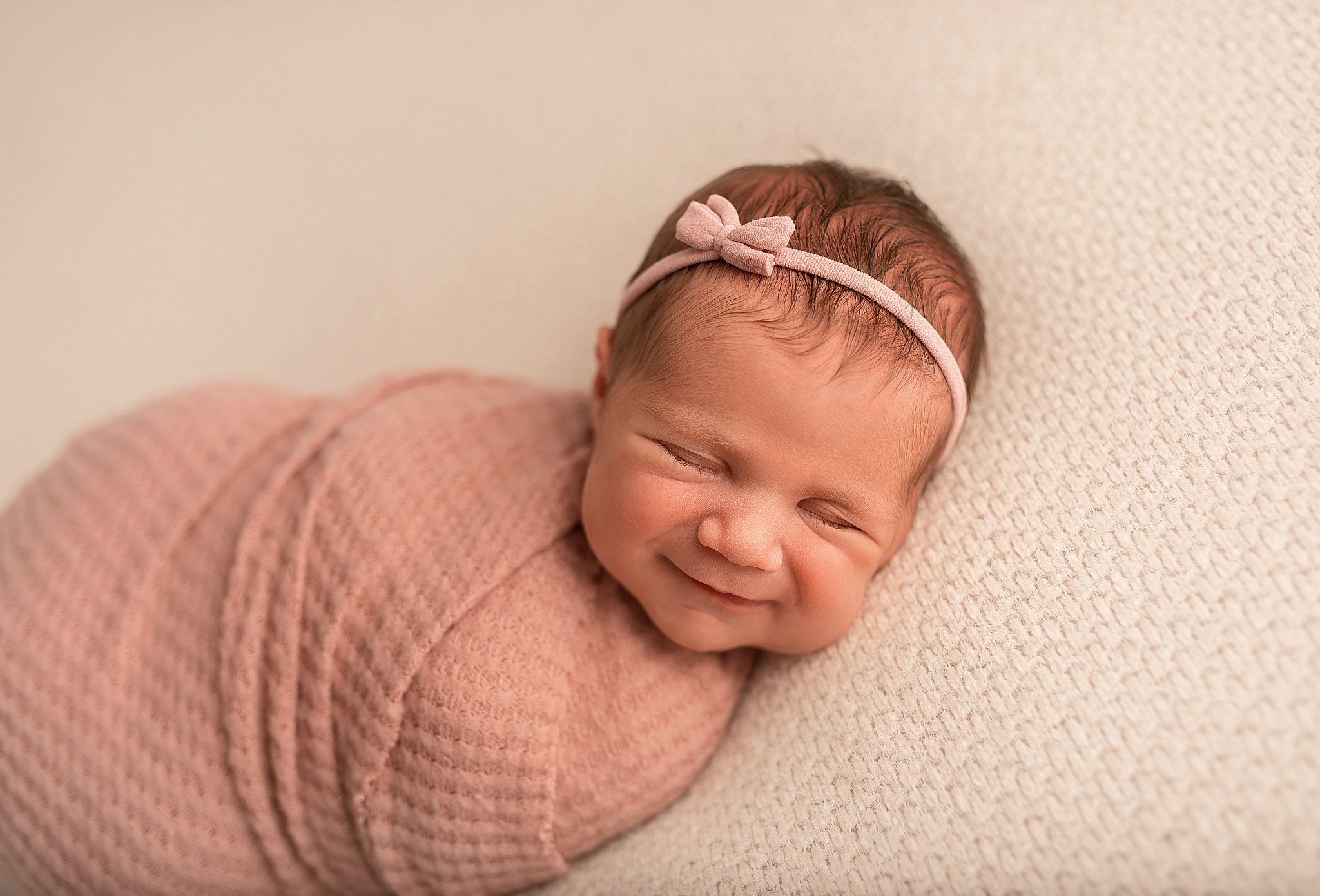 A newborn baby smiles in her sleep in a pink bow headband The nanny connection