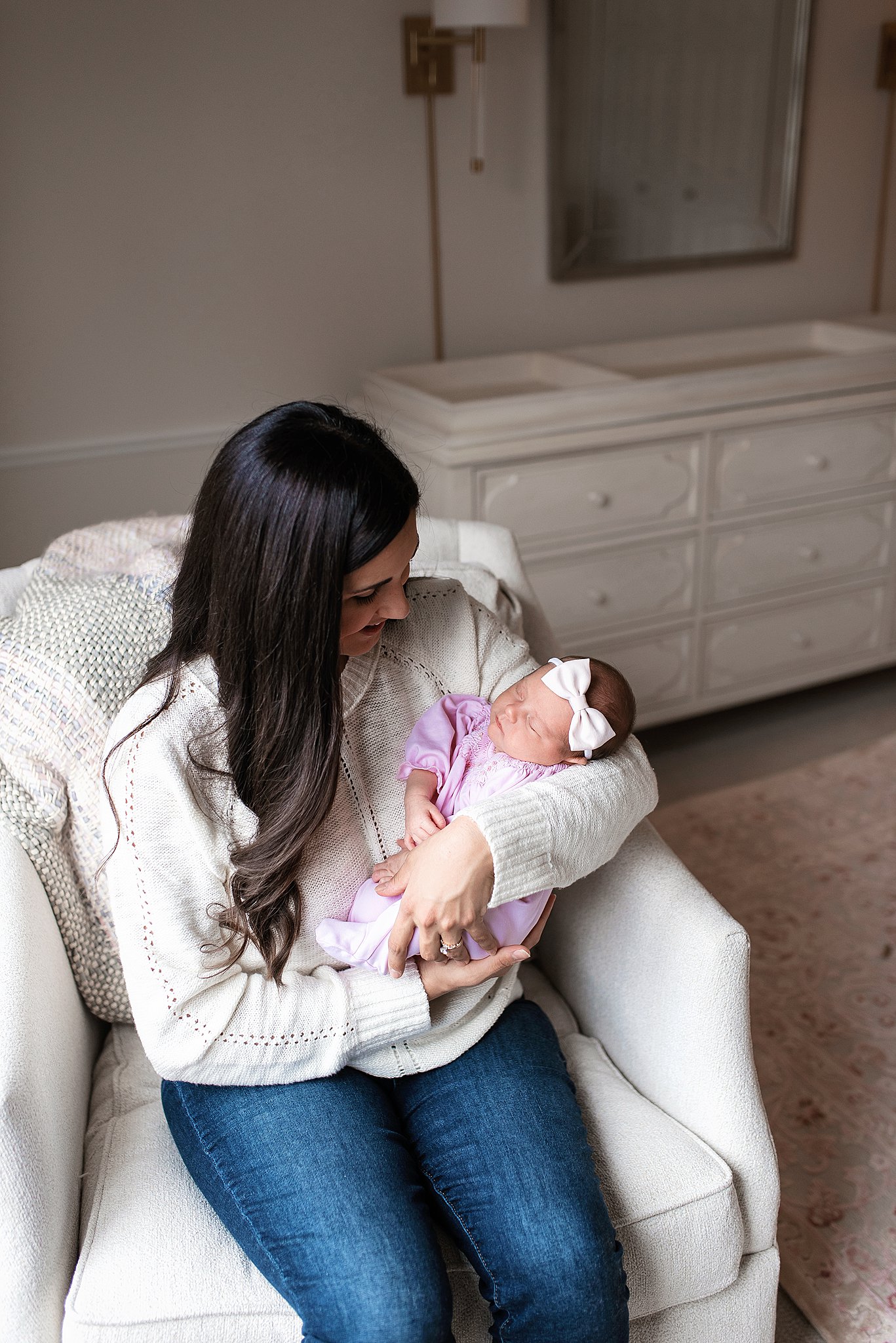 A new mother in a white sweater sits in an armchair holding her sleeping newborn baby baby furniture cleveland