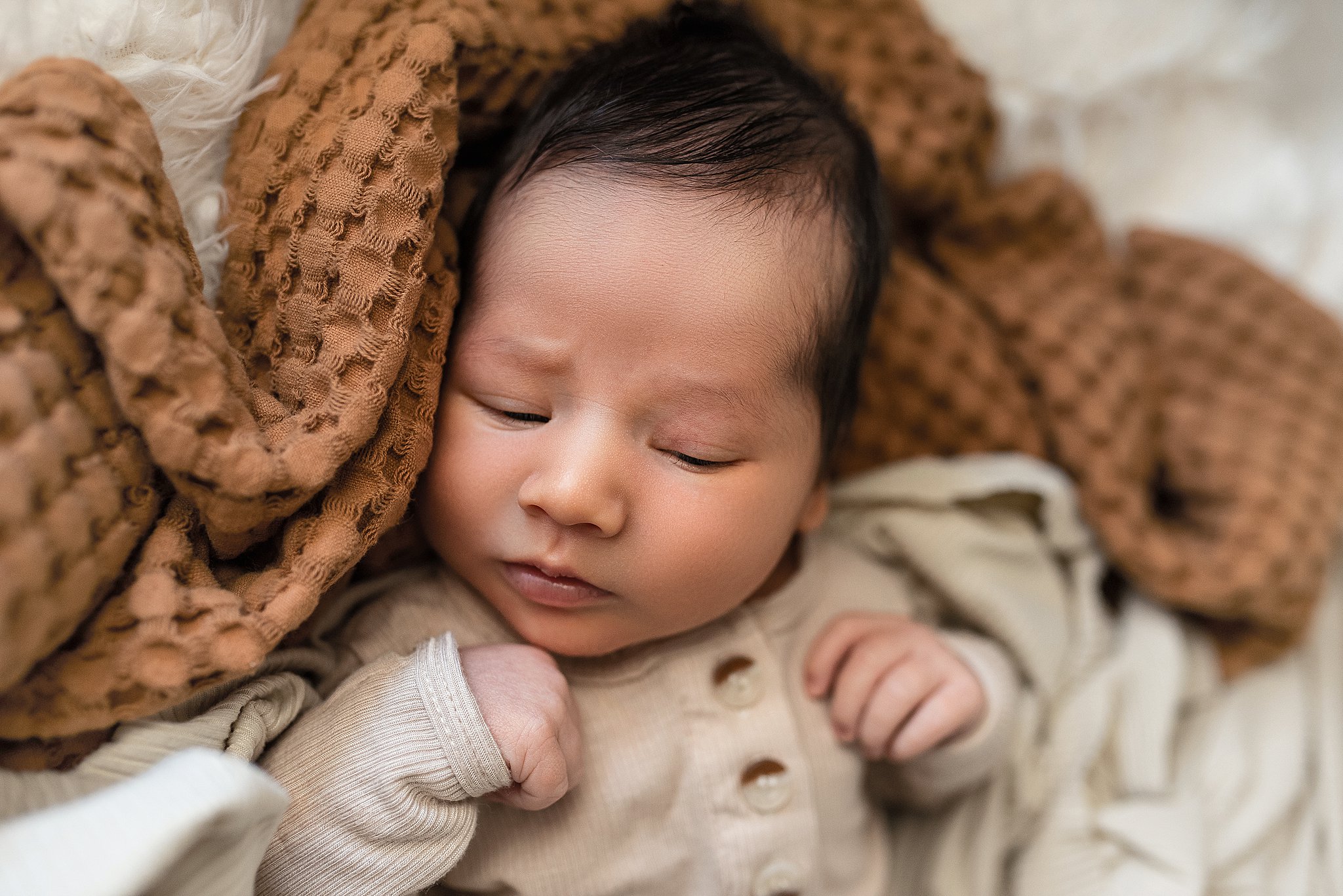 A newborn baby sleeps in a beige onesie in a bed of blankets baby stores cleveland