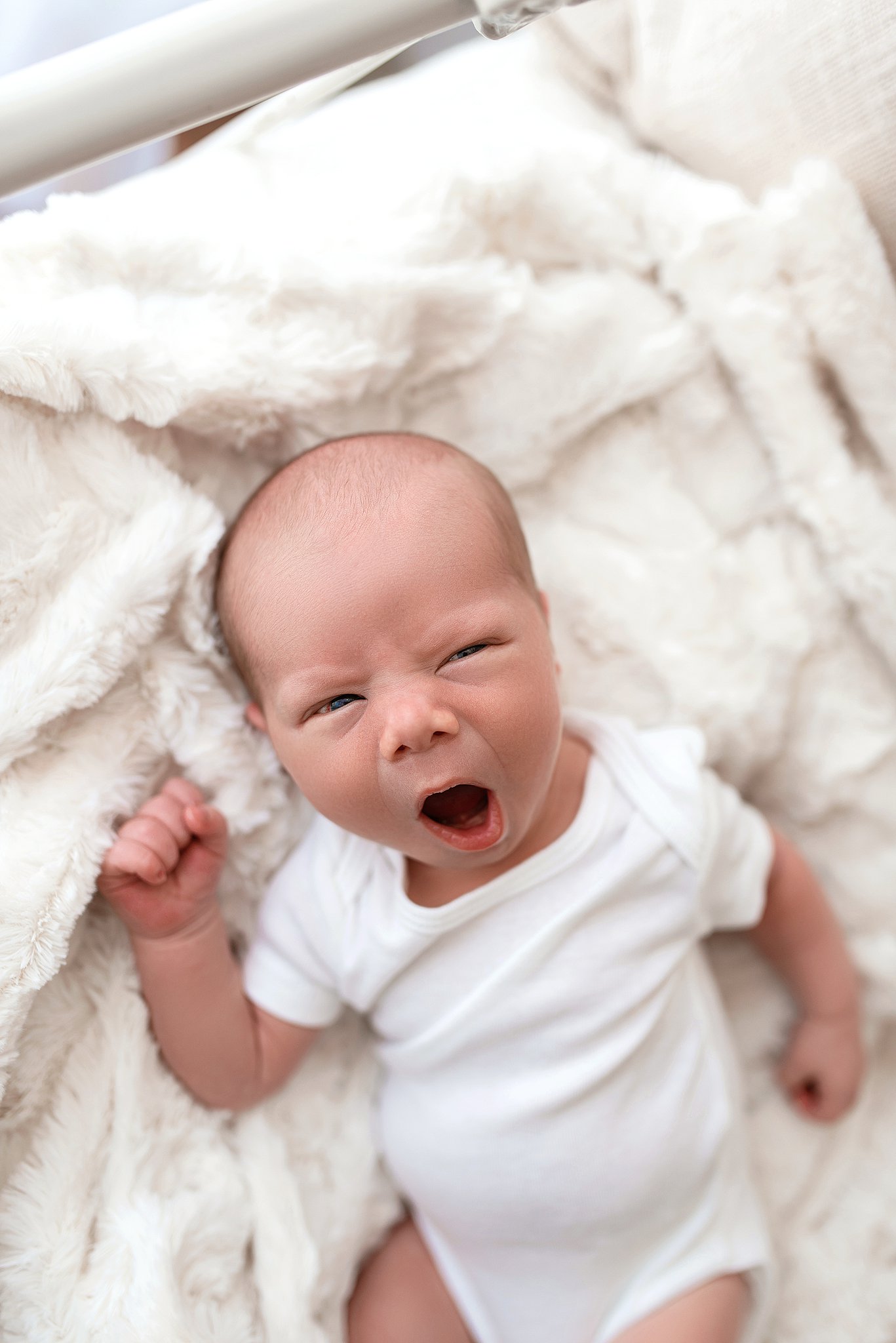 A newborn baby yawns while laying on a soft blanket in a white onesie daycare in cleveland