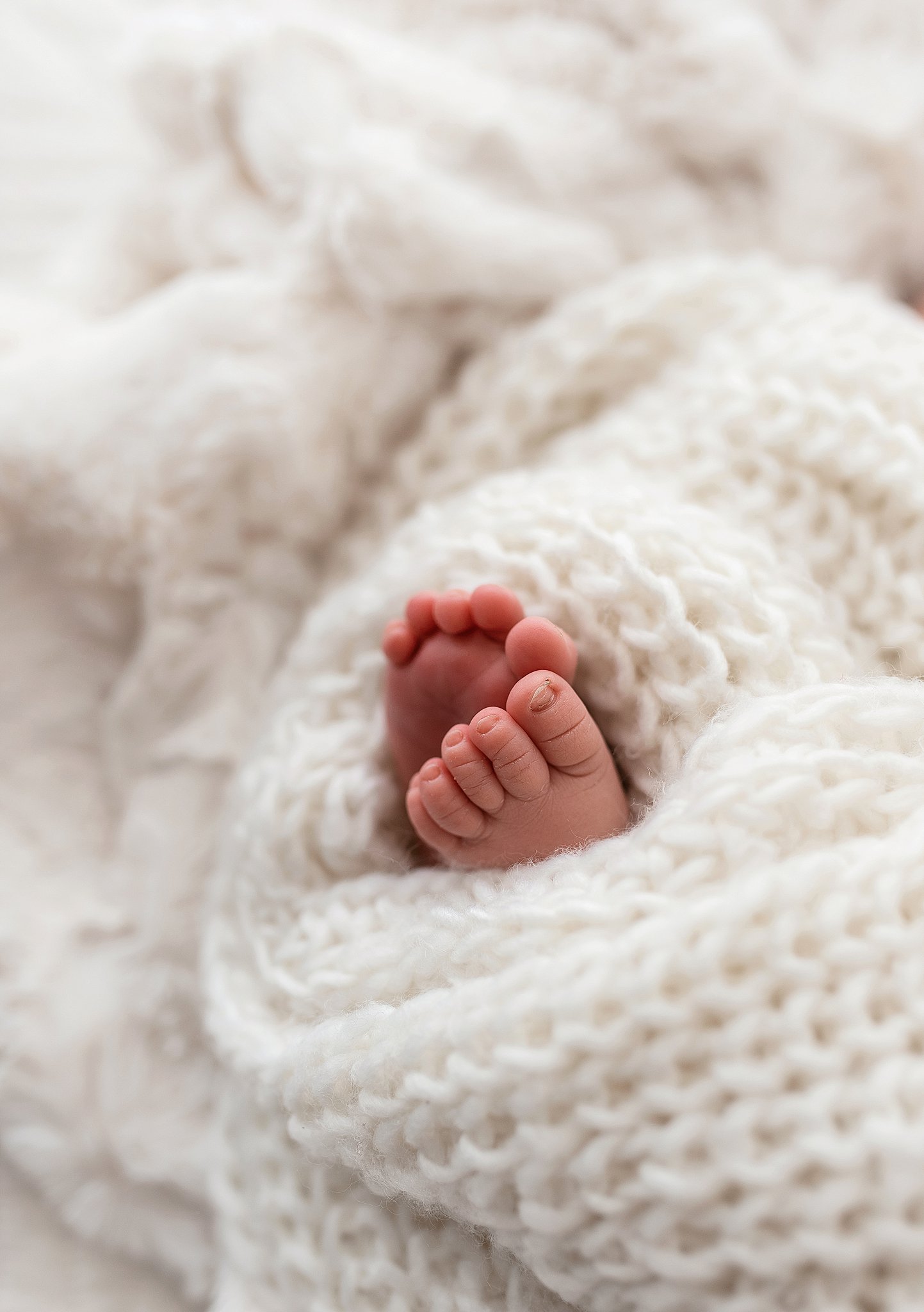 Details of a newborn baby's toes sticking out of a white knit blanket