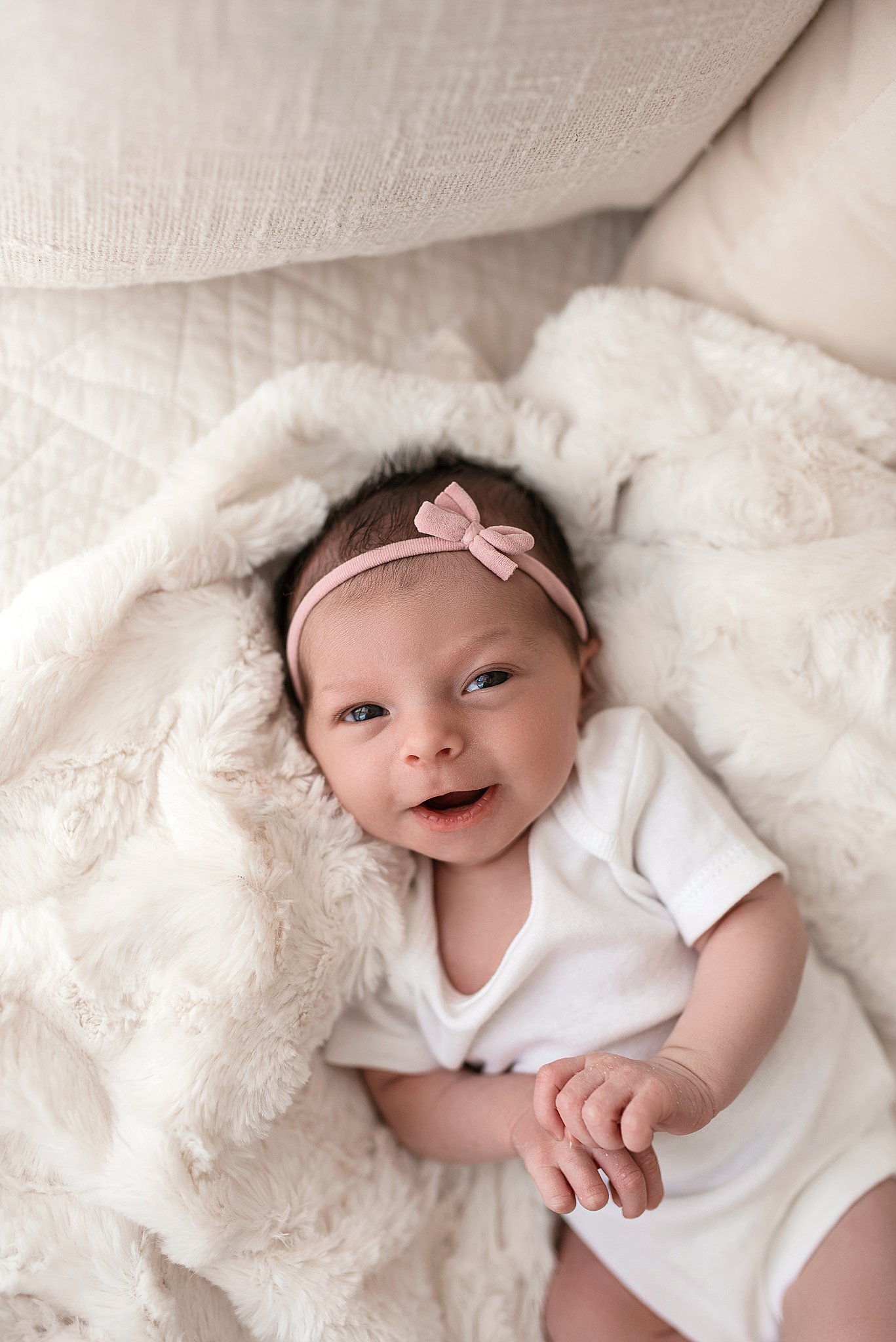 A newborn baby girl smiles with eyes open while laying on a white blanket on a couch night nanny cleveland